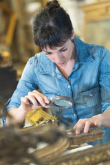 woman using a magnifying glass to inspect a frame embellishment