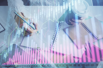 Financial forex graph displayed on hands taking notes background. Concept of research. Multi exposure
