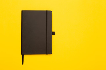 Black notebook isolated on yellow background. Flat lay or Top view angle.
