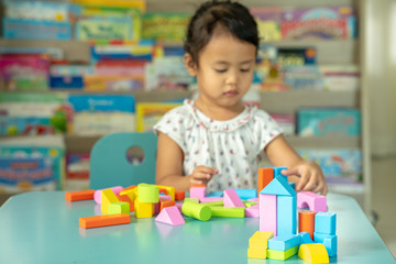 Fototapeta na wymiar Cute little girl playing with multicolor wooden building blocks on blue table.