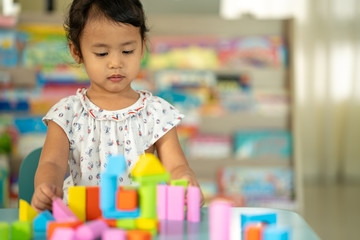 Cute little girl playing with multicolor wooden building blocks on blue table.