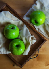 Still life of fruit, with 3 green apples on a wooden tray. Closeup and depth of field