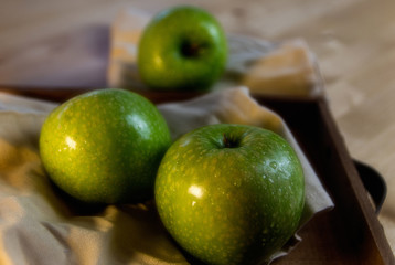 Still life of fruit, with 3 green apples on a wooden tray. Closeup and depth of field