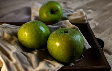 Still life of fruit, with 3 green apples on a wooden tray. Closeup and depth of field