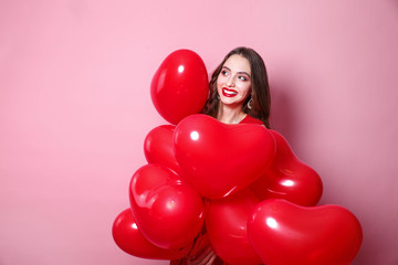 Beautiful elegant young woman with heart shape red air balloons on pink background.