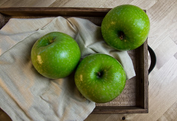 Still life of fruit, with 3 green apples on a wooden tray. Closeup and depth of field