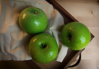 Still life of fruit, with 3 green apples on a wooden tray. Closeup and depth of field