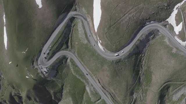 Aerial view of cars driving on winding road in mountains. Kazbegi, Georgia. People flying on paraglider or paraplane. Summer landscape. Snow lies in parts on the ground. Travel motivation. Journey.