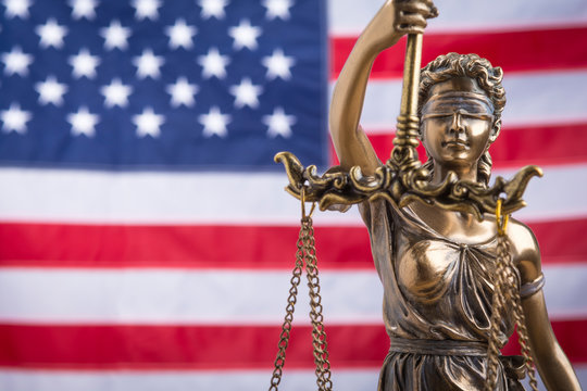 The statue of justice Themis or Iustitia, the blindfolded goddess of justice against a flag of the United States of America, as a legal concept