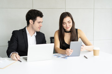 Beautiful young business woman and handsome businessman in formal suits discussing while using digital tablet in modern office.Busienss teamwork concept. - Powered by Adobe