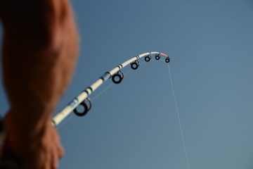 Hand holding fishing rod and reel against the sky