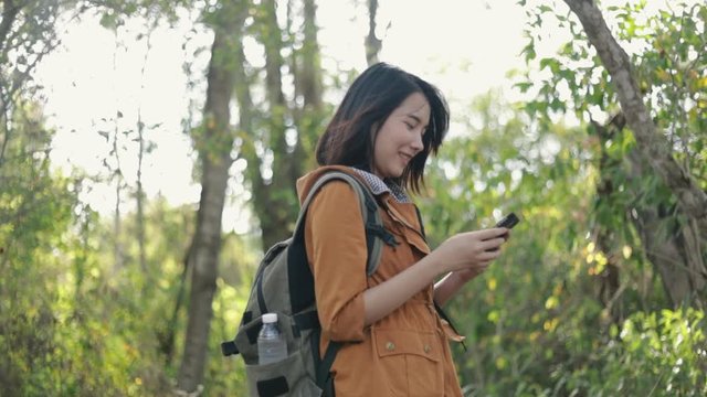 Smiling young Asian woman tourists using smartphones in the forest on sunny beautiful summer and enjoy the vacation lifestyle.