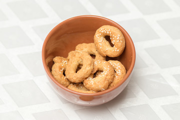 Round and savory pretzel, crispy dough, Middle Eastern Arab style, coated with sesame seeds, in a red clay bowl, on a blurred white background.