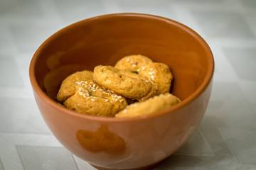 Round and savory pretzel, crispy dough, Middle Eastern Arab style, coated with sesame seeds, in a red clay bowl, on a blurred white background.