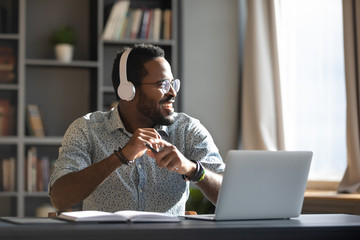 Happy millennial african businessman wear headphones listening music in office