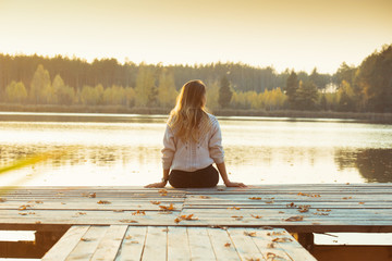 A young slender blonde sits on a wooden pier with her back .