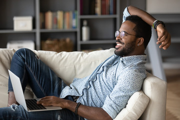 Relaxed african man resting on couch using laptop at home