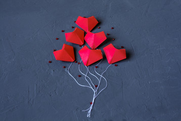 Origami red hearts made of paper on a dark blue background laid out in the form of balloons. Valentine day.