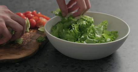 man hands preparing salad with mozzarella, cherry tomatoes and frisee leaves in white bowl on terrazzo surface