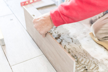 Man installing rectangular shaped floor tiles in kitchen. Applying adhesive before installation and verifying afterwards