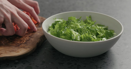 man hands preparing salad with mozzarella, cherry tomatoes and frisee leaves in white bowl on terrazzo surface