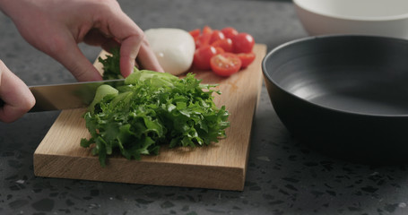 man hands preparing salad with mozzarella, cherry tomatoes and frisee leaves in black bowl on terrazzo surface
