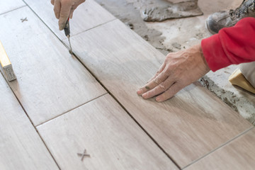 Man installing rectangular shaped floor tiles in kitchen. Applying adhesive before installation and verifying afterwards