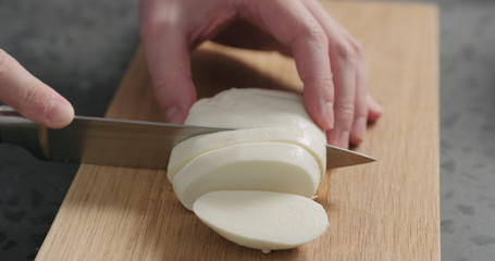 Closeup man slicing fresh mozzarella on oak board
