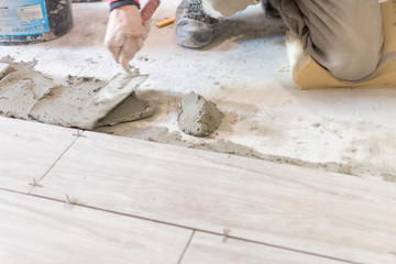 Man installing rectangular shaped floor tiles in kitchen. Applying adhesive before installation and verifying afterwards