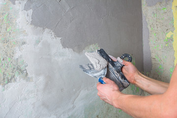 Repair the wall. Plaster the wall with a spatula. Internal construction and finishing works. The Builder puts plaster on the wall .Hand holding a spatula with construction mix and smoothes out bumps.