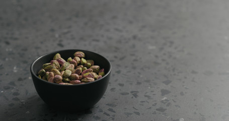 peeled pistachios in black bowl on terrazzo surface