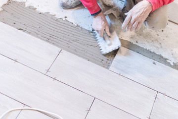 Man installing rectangular shaped floor tiles in kitchen. Applying adhesive before installation and verifying afterwards