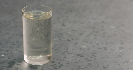 pour transparent sparkling drink in glass on terrazzo surface with copy space