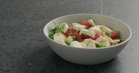 add olive oil to salad with mozzarella, cherry tomatoes and frisee leaves in white bowl on terrazzo surface