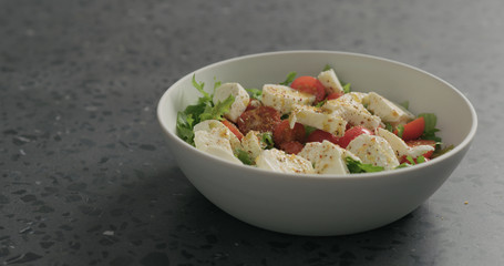 ground spices to salad with mozzarella, cherry tomatoes and frisee leaves in white bowl on terrazzo surface