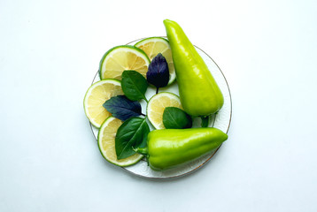 Green peppers on a plate, decorated with slices of lime and leaves of basil.