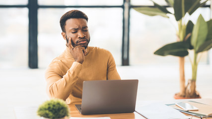 Focused black man working with laptop at office
