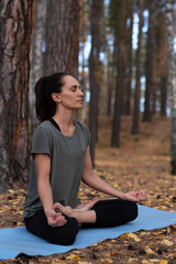 Beautiful dark-haired woman meditating in a pine forest with her eyes closed