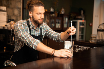 Bearded bartender is putting ice in a glass