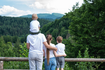 Fototapeta na wymiar Mother, father and two children on nature background. Rest of the city. Back view