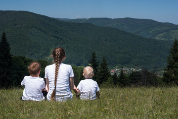 Mother with children resting in meadow. Nanny with kids during the journey. Back view