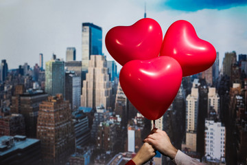 Valentines day in the New York city. man and woman hands holding three red balloons in form of heart over Manhattan and skyscrapers. Сoncept. America. USA. Aerial view.