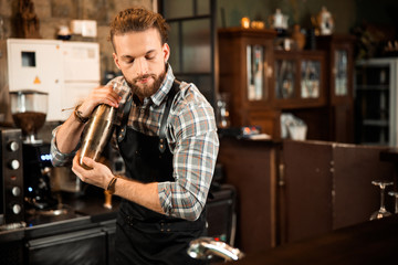 Smiling handsome bartender making cocktail in shaker