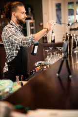 Bearded young bartender standing and making drink