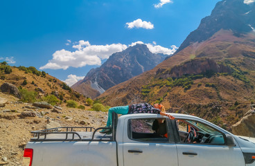 Beautiful young lies on the roof of a pickup truck on the background of the beautiful mountains of Tajikistan