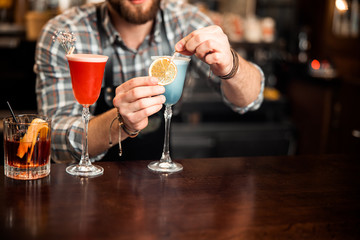 Obraz na płótnie Canvas Barman decorating cocktail with a slice of orange