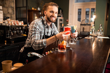 Happy bartender is offering two colorful cocktails