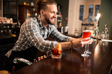 Happy bartender is looking on two colorful cocktails