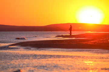 Beautiful golden sunset on the beach with fishermen and kitesurfers