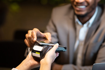 Afro businessman paying with mobile phone at bar